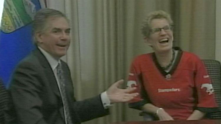 Alberta Premier Jim Prentice with Ontario Premier Kathleen Wynne, who is wearing a Calgary Stampeders jersey; Toronto, December 3, 2014