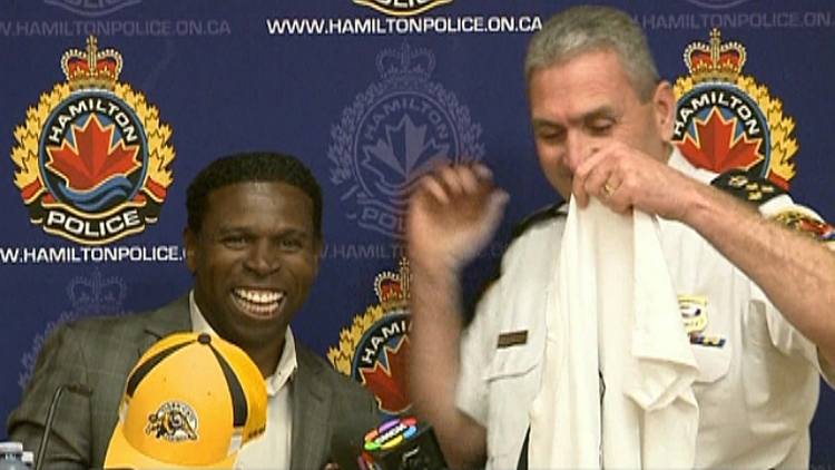 Michael 'Pinball' Clemons holds a Hamilton Tiger-Cats cap as Hamilton Police Chief Glenn De Caire holds up a 'Just Give' t-shirt; May 29, 2015