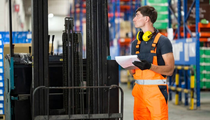 Male Maintenance technician or forklift driver is checking battery restraints are functional and record checklist report at a factory warehouse.