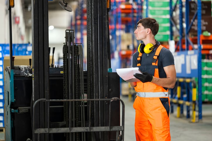 Male Maintenance technician or forklift driver is checking battery restraints are functional and record checklist report at a factory warehouse.